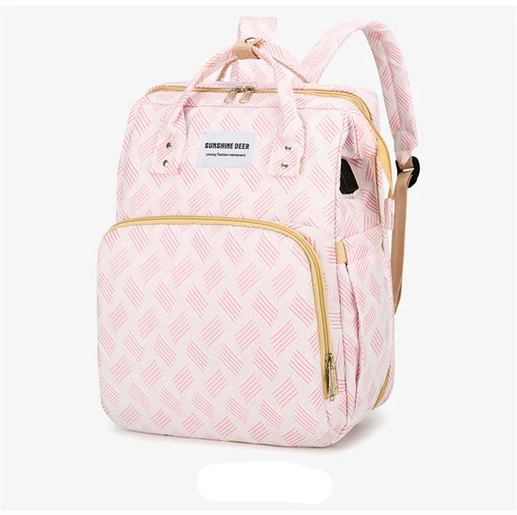 Vue trois quarts du sac a langer rose au motif texture avec finitions dorees, presente sur fond blanc.
