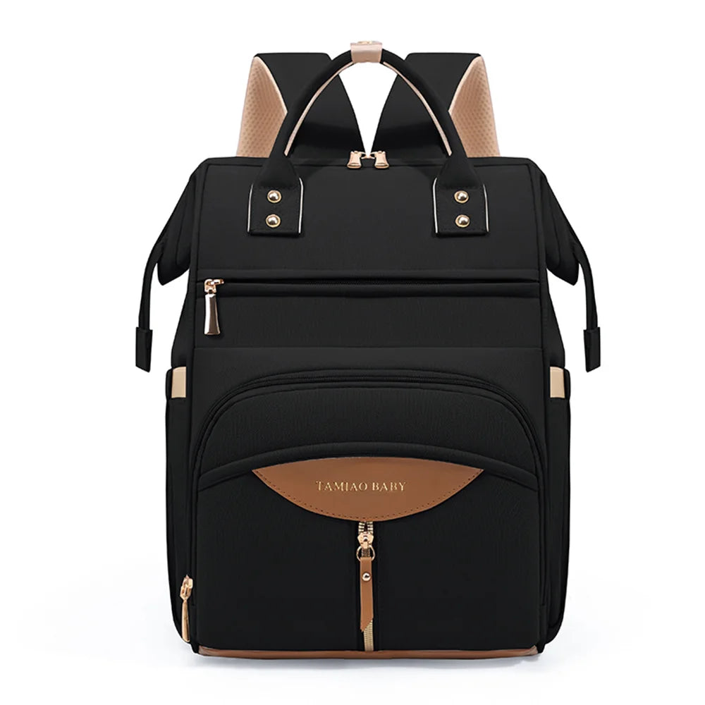 Sac a dos a langer noir aux finitions cognac et dorees, ideal pour transporter les affaires de bebe avec style au quotidien
