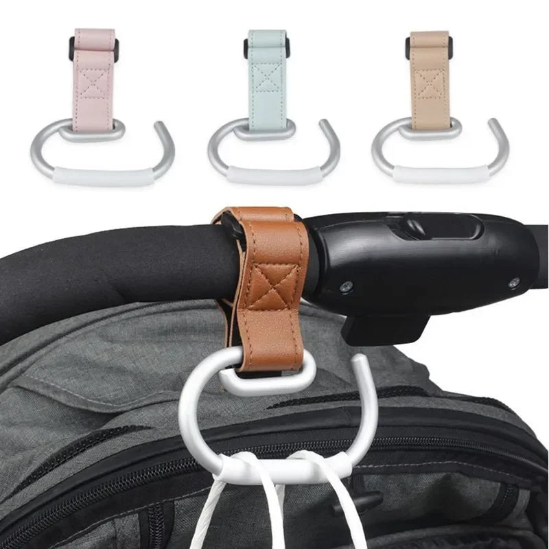 Gamme de trois attaches poussette rose, vert et beige, une fixee sur un guidon retenant un sac a dos volumineux.