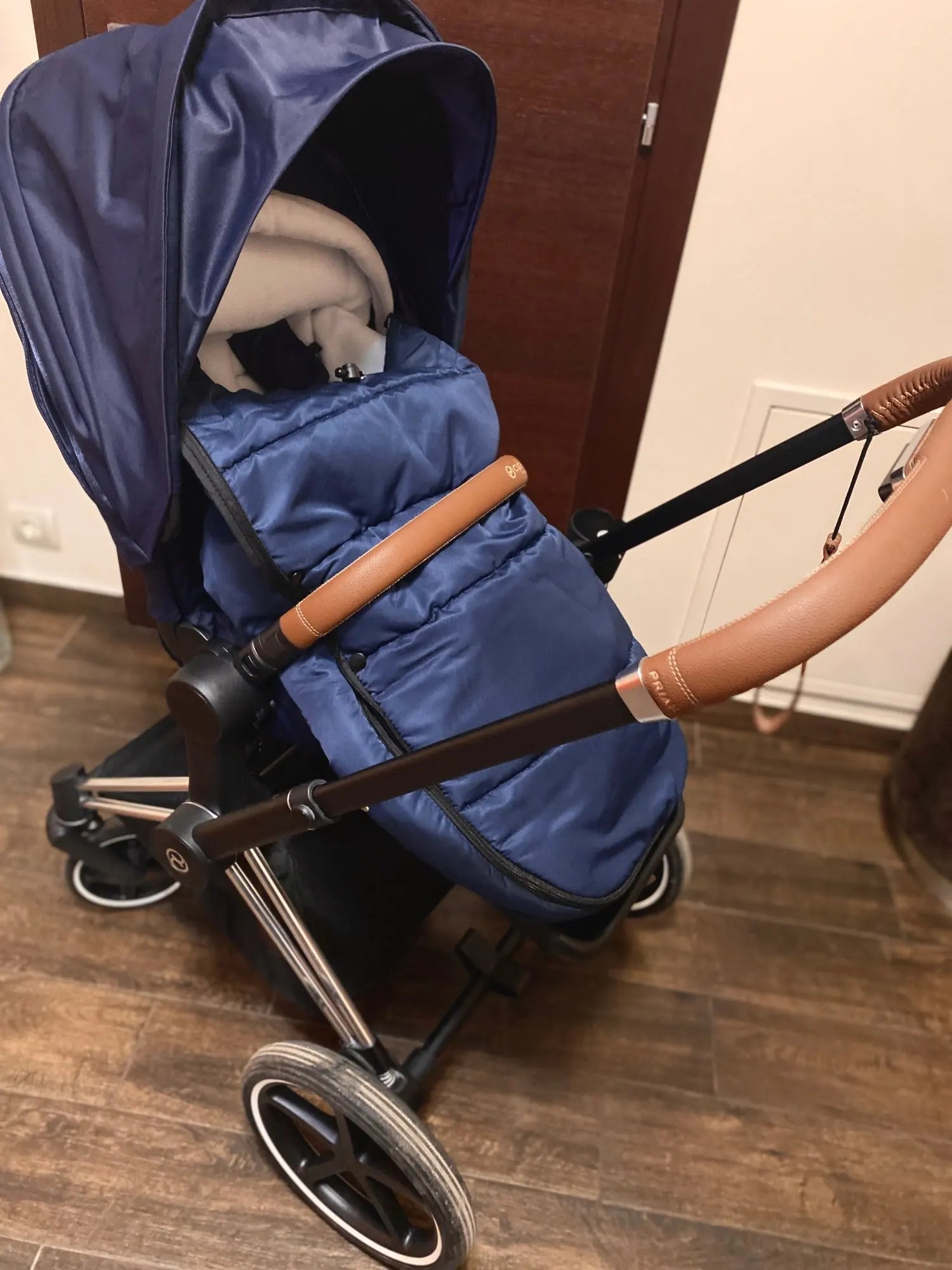 Chanceliere fixee sur une poussette Cybex Priam avec poignee cuir, prete pour une sortie hivernale confortable.
