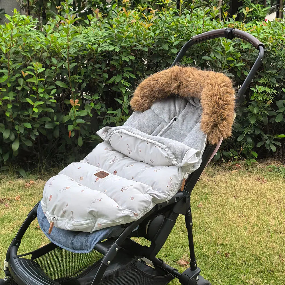 Chanceliere grise motif oie installee et depliee sur une poussette, montrant sa grande surface matelassee pour tenir bebe au chaud.
