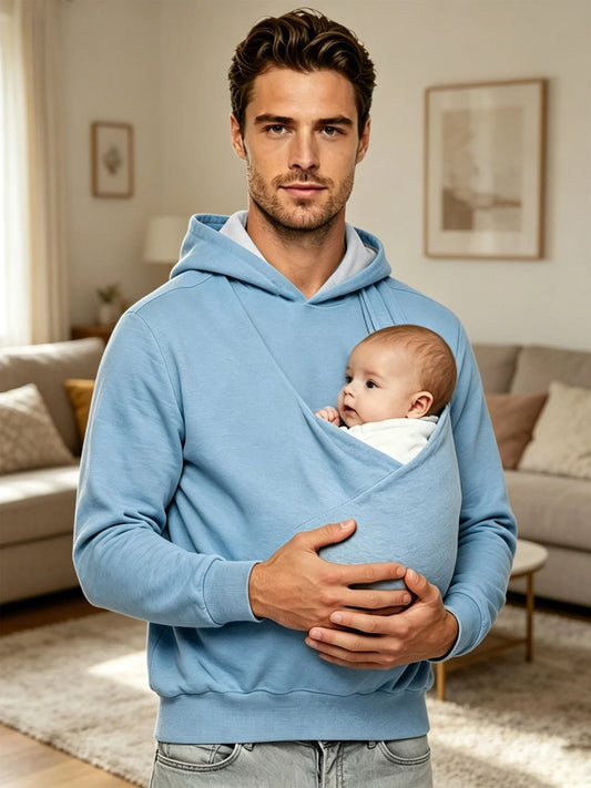 Papa a la maison portant son bebe en peau contre peau dans le manteau bleu, gardant les mains libres et l'enfant au chaud.