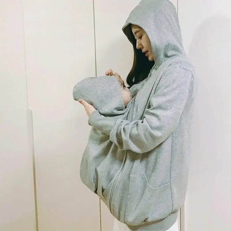 Le manteau de portage protege la tete du bebe avec sa capuche integree pendant que la maman le berce contre elle.