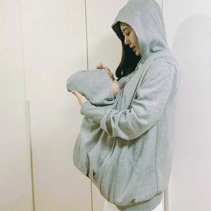 Le manteau de portage protege la tete du bebe avec sa capuche integree pendant que la maman le berce contre elle.