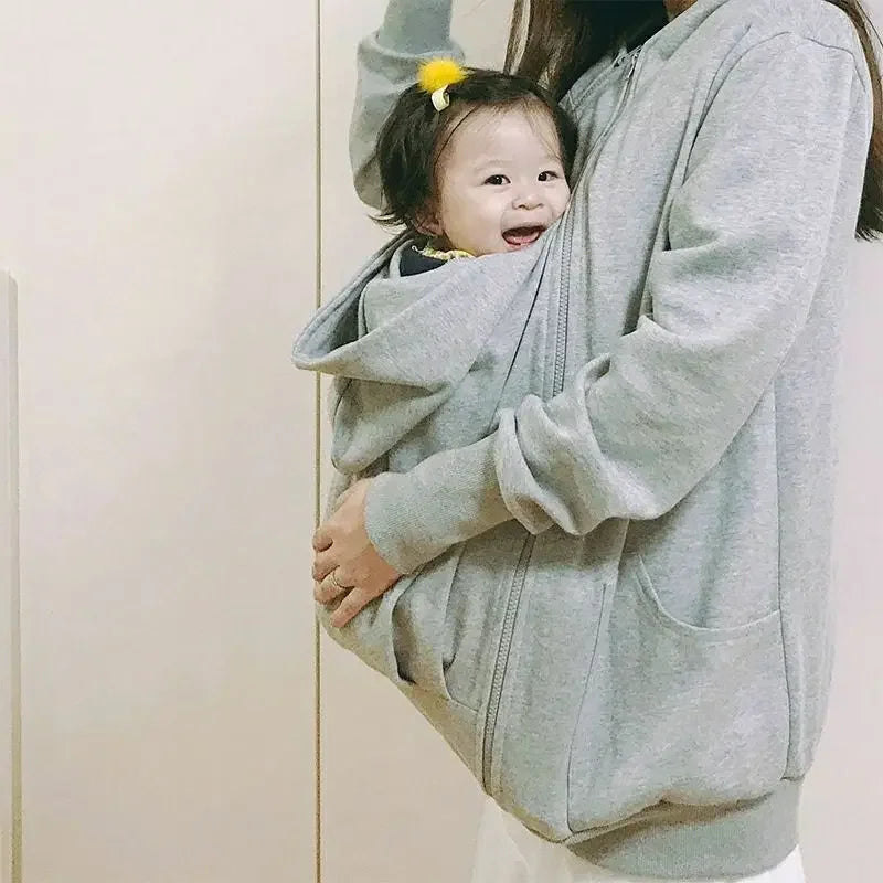 Bebe eveille et souriant dans la poche de portage, bien maintenu contre le ventre de sa maman.