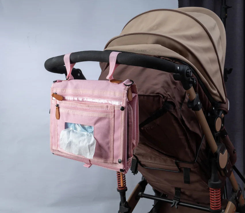 Version rose du matelas a langer suspendue a la barre de poussette avec fenetre d'acces aux lingettes pour un change express