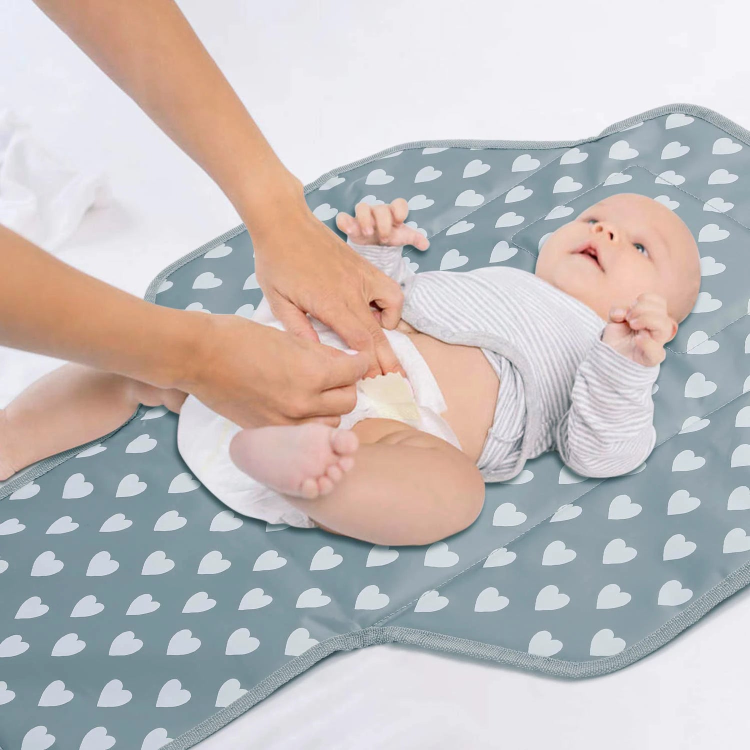 Parent changeant la couche de son bebe sur le matelas a langer portable, illustrant sa praticite lors des sorties et voyages.