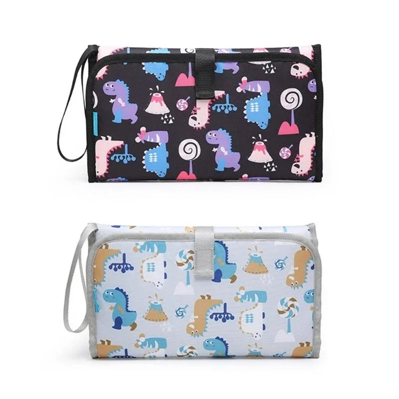Presentation des deux coloris disponibles du matelas a langer nomade, un fond noir et un fond bleu clair a motifs dinosaures.