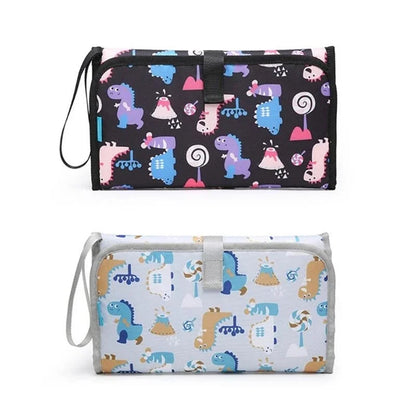 Presentation des deux coloris disponibles du matelas a langer nomade, un fond noir et un fond bleu clair a motifs dinosaures.