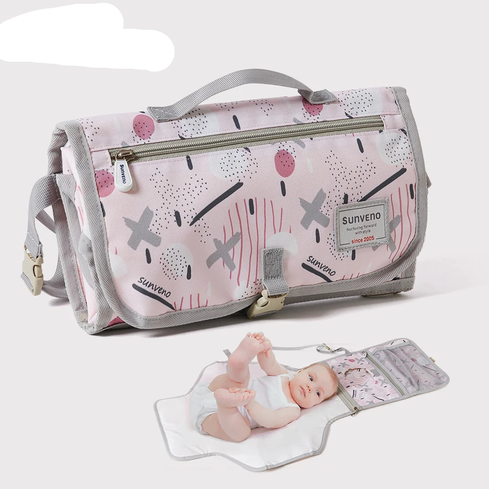 Matelas a langer nomade Sunveno replie en pochette compacte avec bebe installe sur le tapis deplie pret pour le change en deplacement.