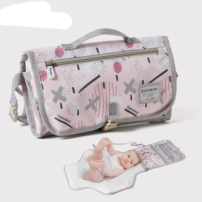 Matelas a langer nomade Sunveno replie en pochette compacte avec bebe installe sur le tapis deplie pret pour le change en deplacement.