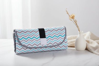 Matelas a langer nomade referme en pochette motif chevron bleu, compact et pratique a emporter partout.