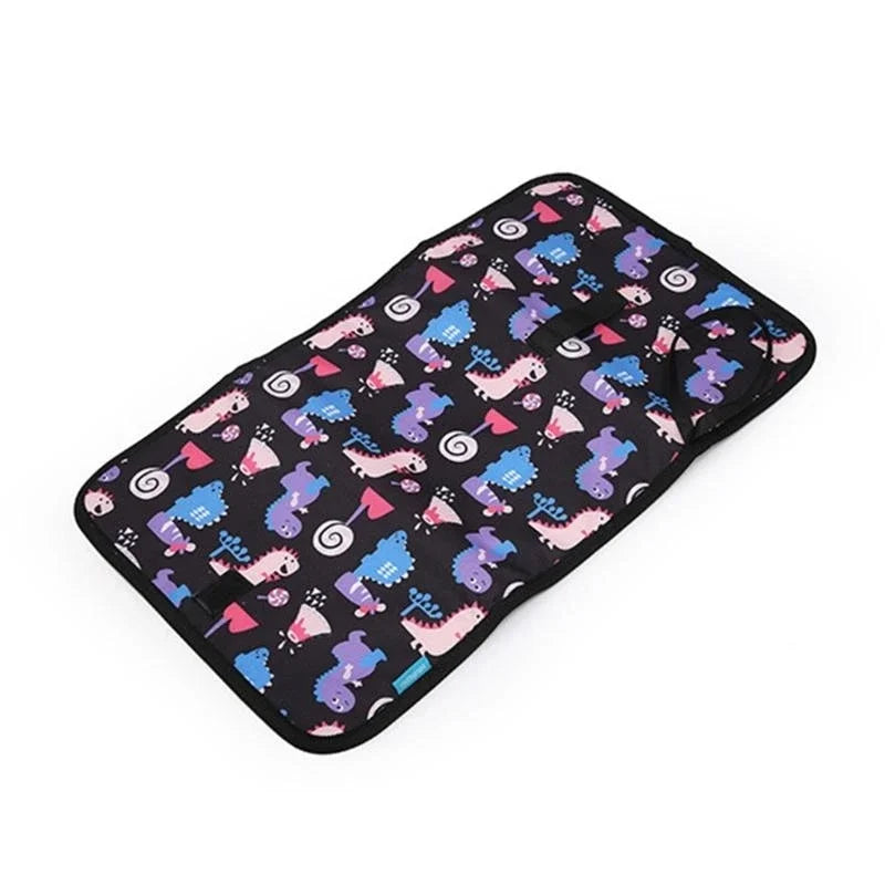 Matelas a langer nomade entierement deplie avec son motif dinosaures colore, offrant une surface propre pour changer bebe partout.