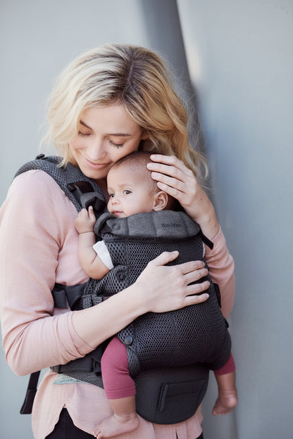 Porte bebe physio anthracite presente seul et en situation de portage ventral face au parent pour un cocon rassurant.