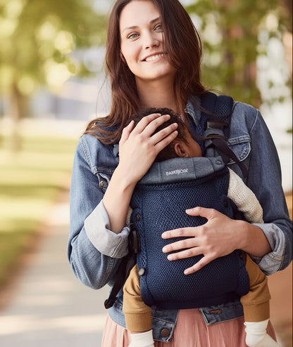 Porte bebe physio bleu marine utilise en exterieur, garantissant un portage tout doux au plus pres du parent.