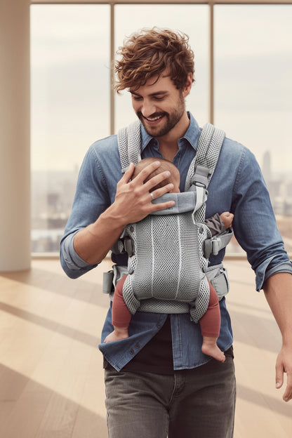 Porte bebe physio gris clair porte par un papa qui protege la tete de bebe d'une main rassurante.