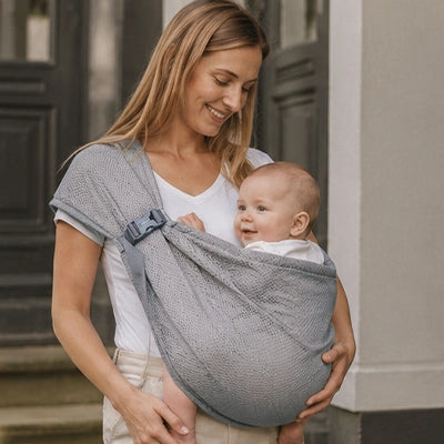 Maman echangeant un sourire avec son bebe positionne face a elle dans le sling gris en maille, position rassurante et confortable.