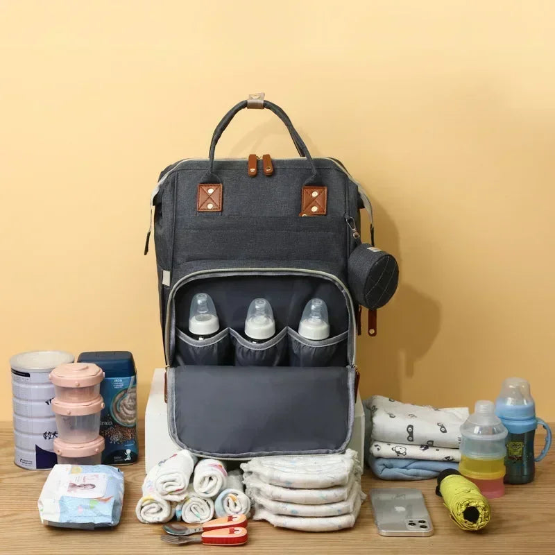 Sac a dos a langer avec lit ouvert montrant ses compartiments isothermes pour biberons et tout le materiel bebe organise autour.