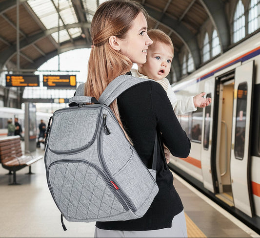 Maman portant le sac a langer a dos tout en tenant son bebe, illustrant la liberte de mouvement au quotidien.