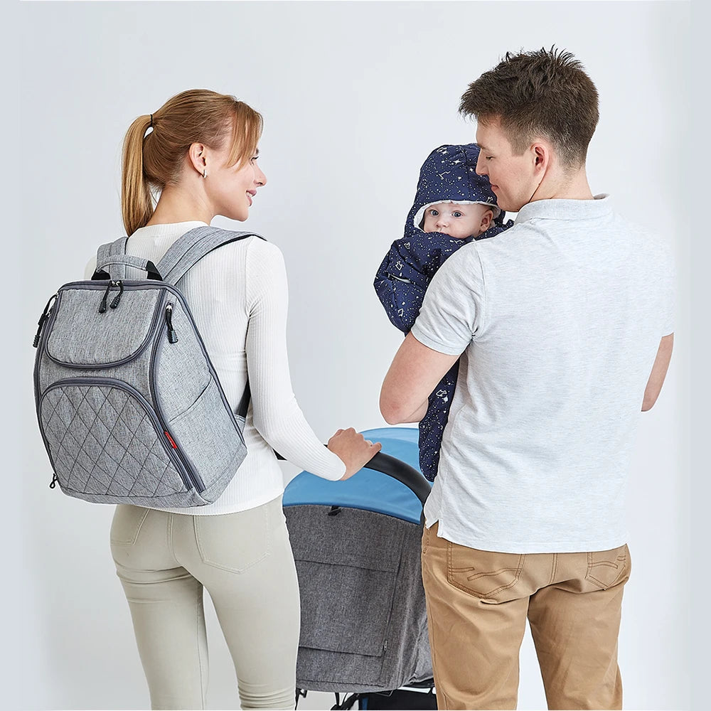 Sac a langer porte par la maman lors d'une sortie en famille, un modele unisexe adapte aux deux parents.