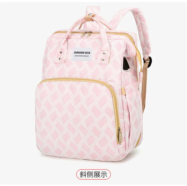 Vue trois quarts du sac a langer rose au motif texture avec finitions dorees, presente sur fond blanc.