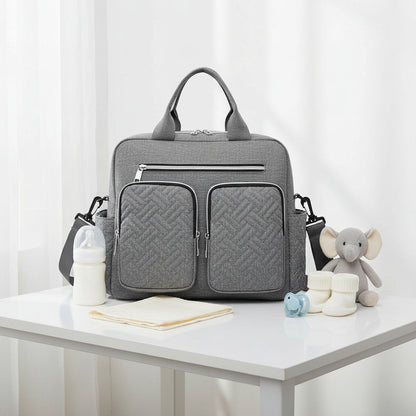 Sac a langer bandouliere gris matelasse presente de face avec ses multiples poches zippees, ideal pour organiser les affaires de bebe au quotidien.