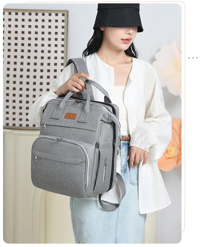 Sac a langer gris porte a l'epaule montrant sa polyvalence entre sac a dos et sac a main.