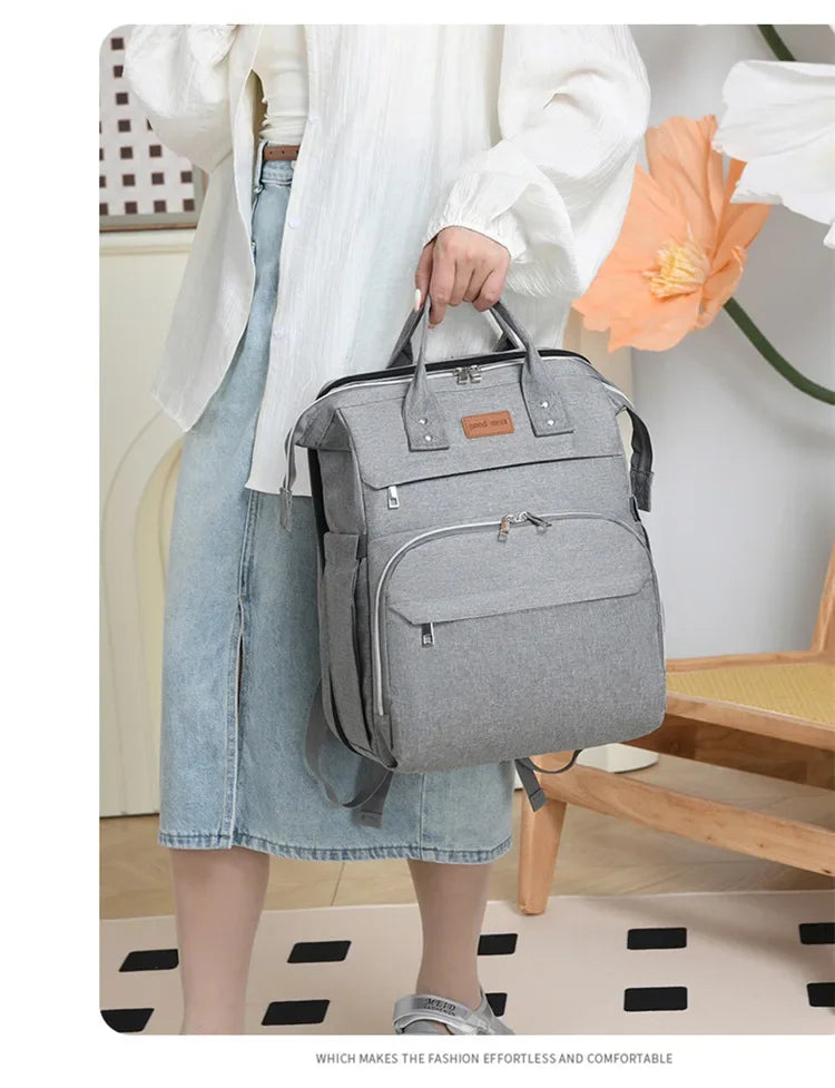 Sac a langer gris porte a la main, elegant et polyvalent pour les rendez-vous en ville.