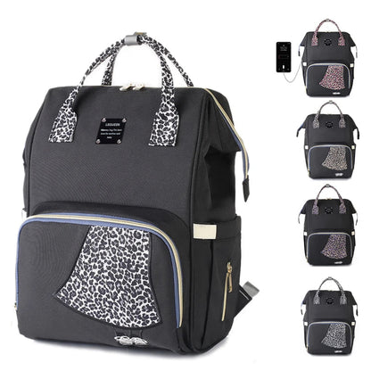 Sac a langer leopard noir decline en plusieurs coloris de motifs, avec port USB integre pour recharger son telephone en deplacement.