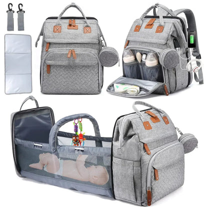 Sac a langer gris equipe d'un port USB, d'une poche isotherme a biberons et d'un berceau depliable avec arceau de jeu pour installer bebe en deplacement.