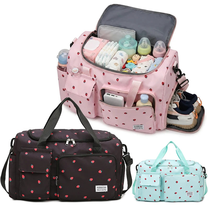 Sac a langer rose motif fraises presente en trois coloris avec grand compartiment ouvert rempli d'affaires de bebe et espace lateral dedie aux chaussures.