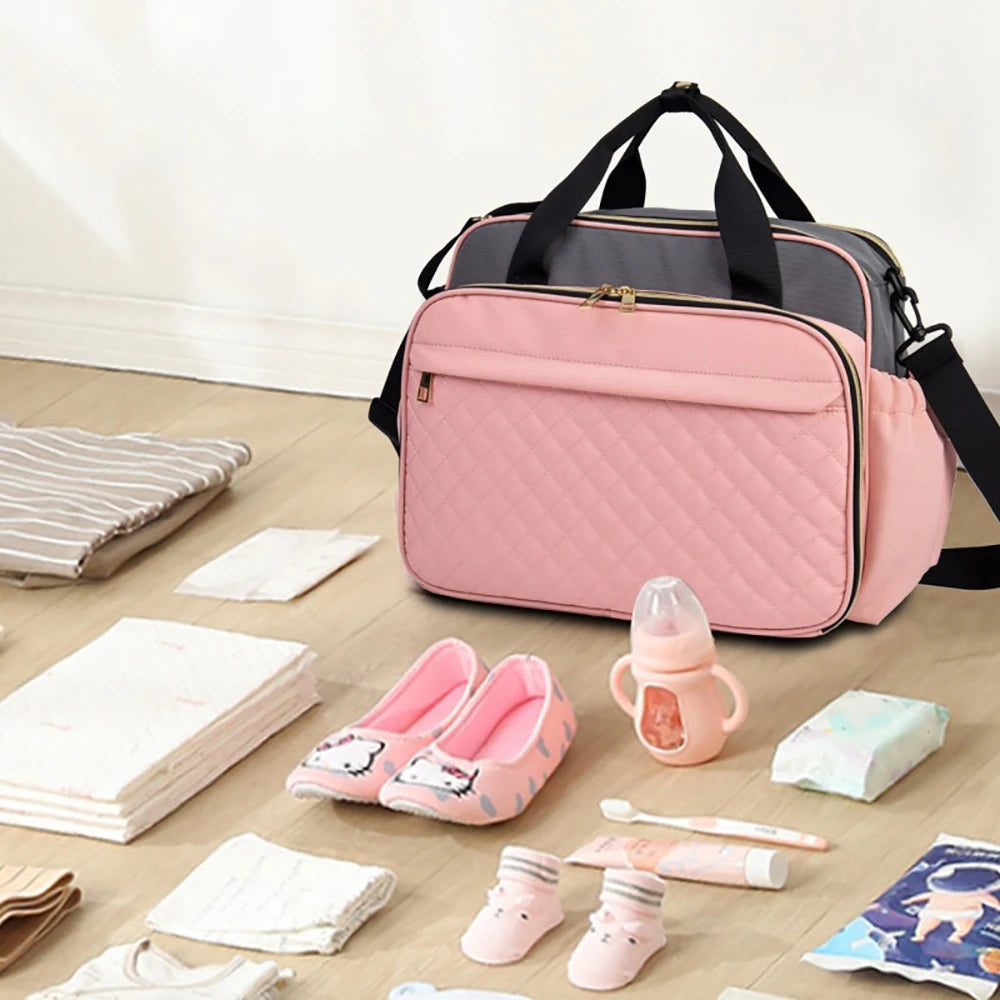 Pose a la maison pres des affaires de bebe, ce sac a langer rose facilite la preparation quotidienne des sorties avec l'enfant.