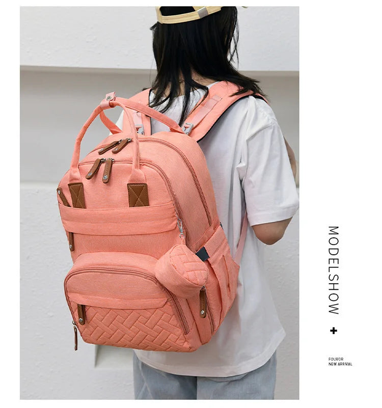 Maman portant le sac a langer rose en mode sac a dos, les mains libres pour s'occuper de bebe lors des sorties quotidiennes.