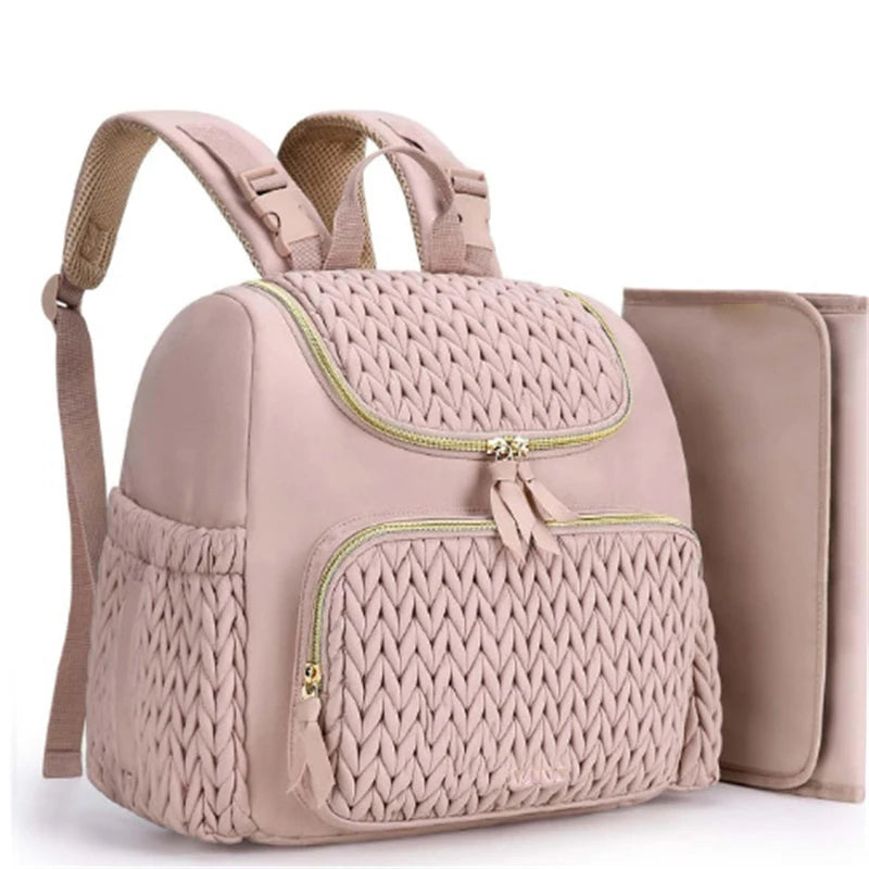 Sac a langer rose au design matelasse elegant presente avec son matelas a langer assorti, port dos confortable pour les parents.