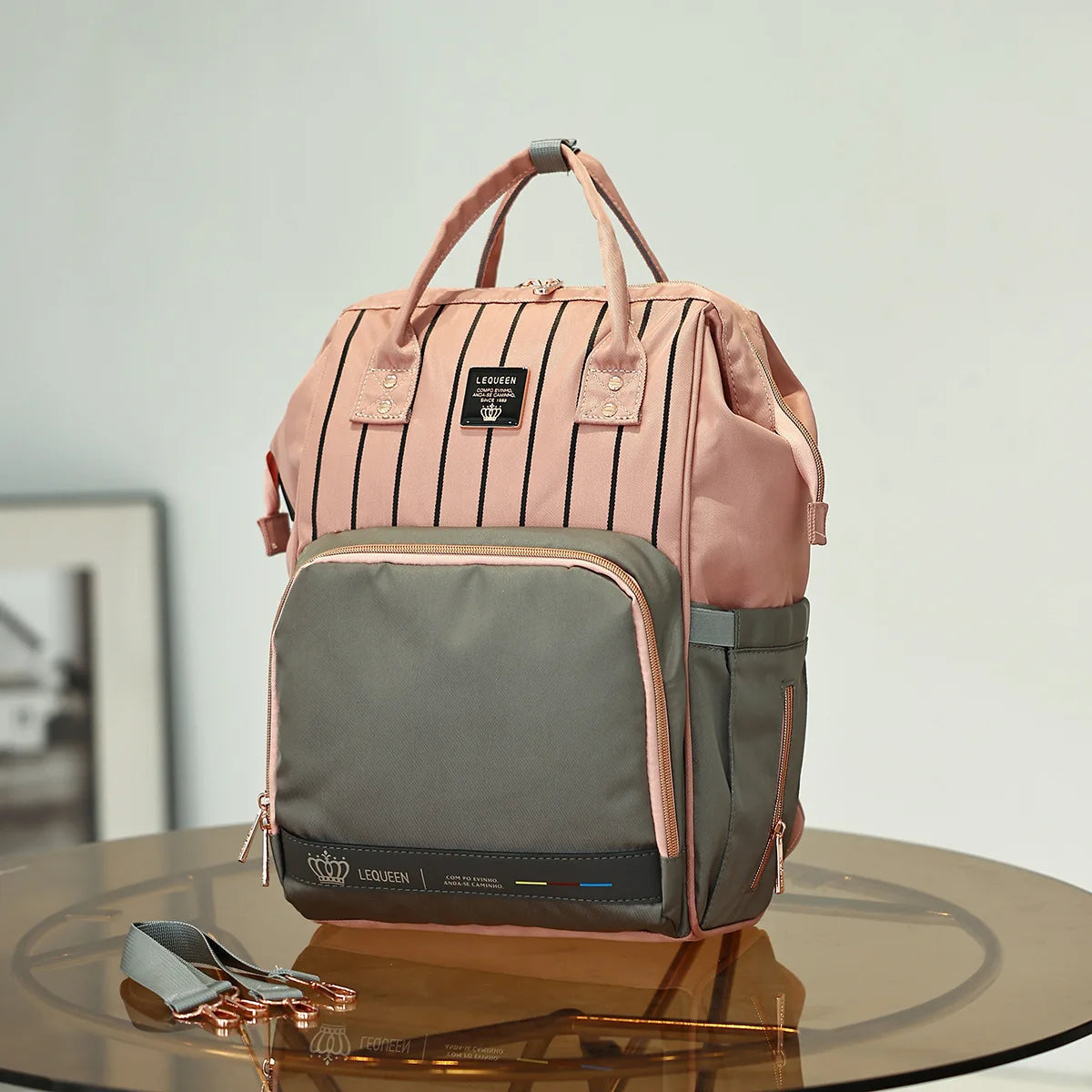 Sac a langer rose et gris a rayures avec finitions dorees, poche a langer premium pour parents elegants en deplacement.