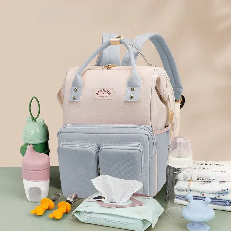 Le sac a langer mis en situation aux cotes des accessoires de bebe qu'il peut contenir : biberons, lingettes, couches et petits ustensiles.