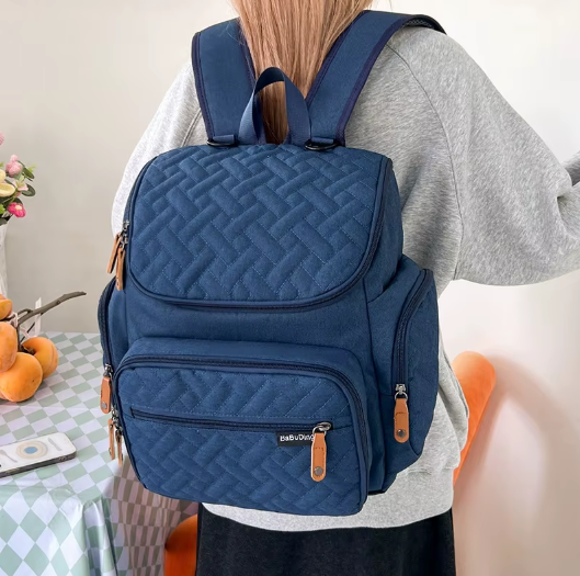 Femme portant le sac a langer sac a dos bleu marine sur les epaules pour un transport confortable et mains libres.