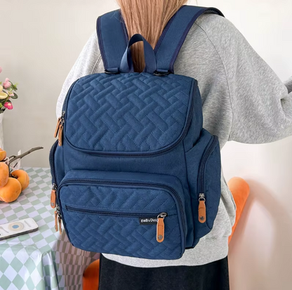 Femme portant le sac a langer sac a dos bleu marine sur les epaules pour un transport confortable et mains libres.