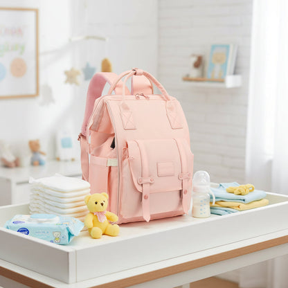 Sac a langer sac a dos rose pose sur une table a langer, entoure de couches, lingettes et biberon pret pour bebe.