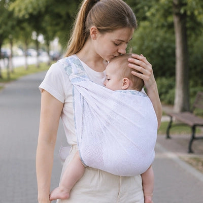 Bebe paisiblement endormi contre sa maman dans le sling en maille, preuve du confort et du maintien offerts lors des sorties.