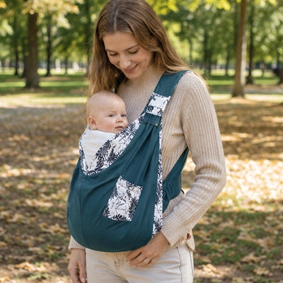 Maman portant son bebe dans le sling lors d'une promenade au parc, les mains totalement libres.