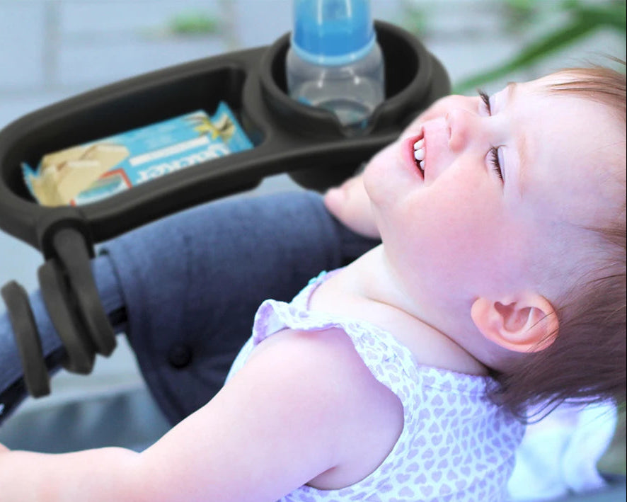 Bebe installe dans sa poussette profite de sa tablette 2-en-1 qui accueille biberon et gouter a portee de main pendant la balade.