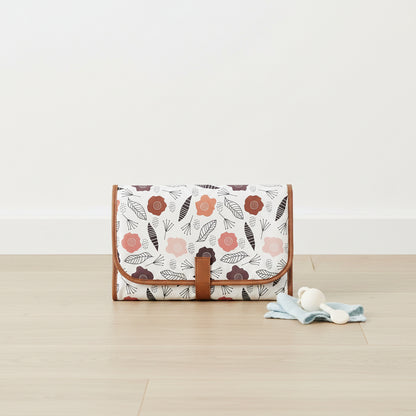 Tapis a langer de voyage impermeable plie dans un imprime floral scandinave sur fond blanc, compact et facile a transporter.
