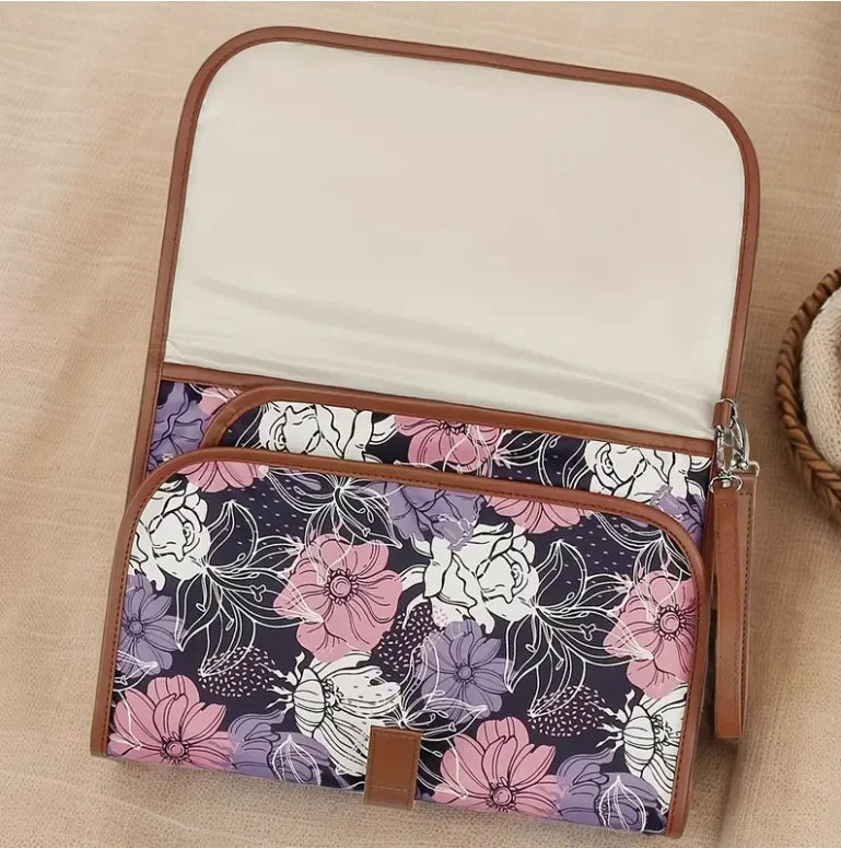 Tapis a langer ouvert montrant sa surface matelassee douce et sa poche de rangement dans un coloris floral violet elegant.