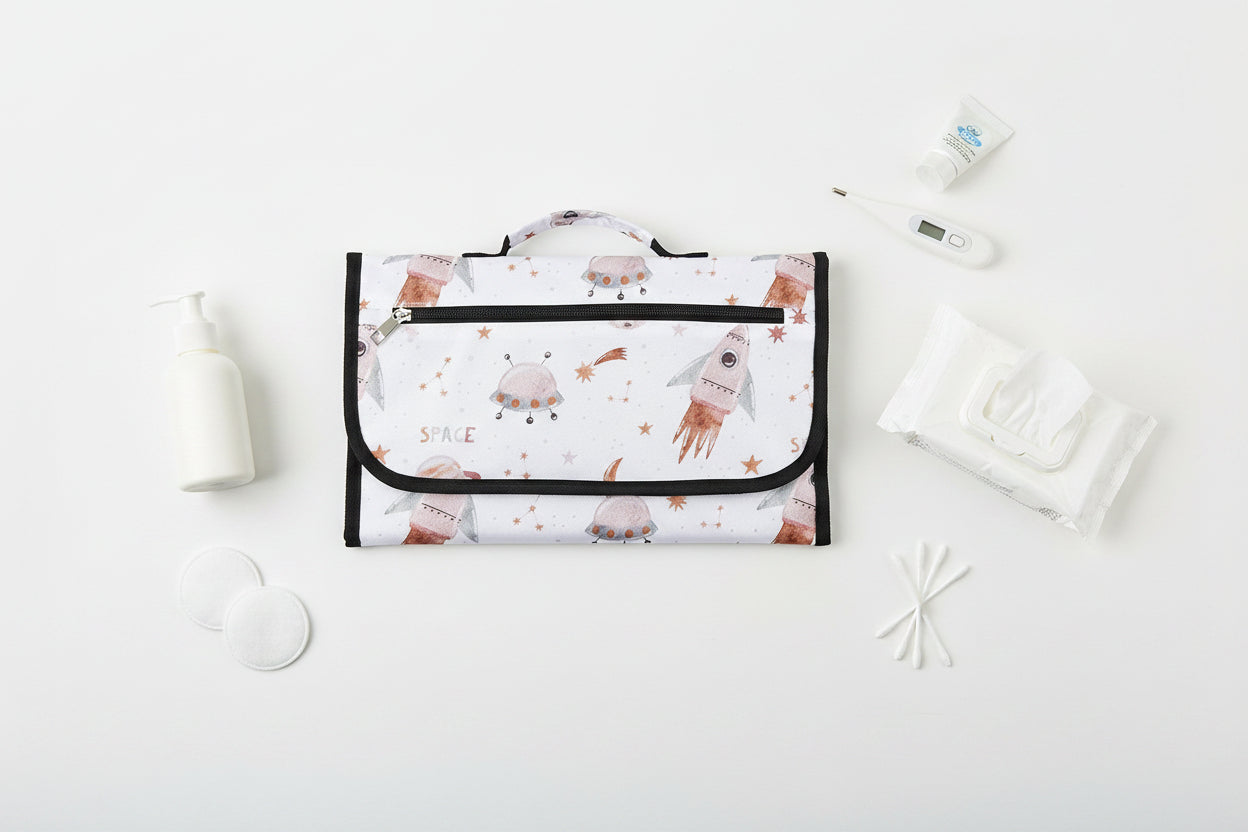 Version compacte du tapis a langer avec imprime espace et fusees, ideale pour ravir bebe lors des changes en deplacement.