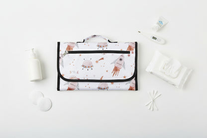 Version compacte du tapis a langer avec imprime espace et fusees, ideale pour ravir bebe lors des changes en deplacement.