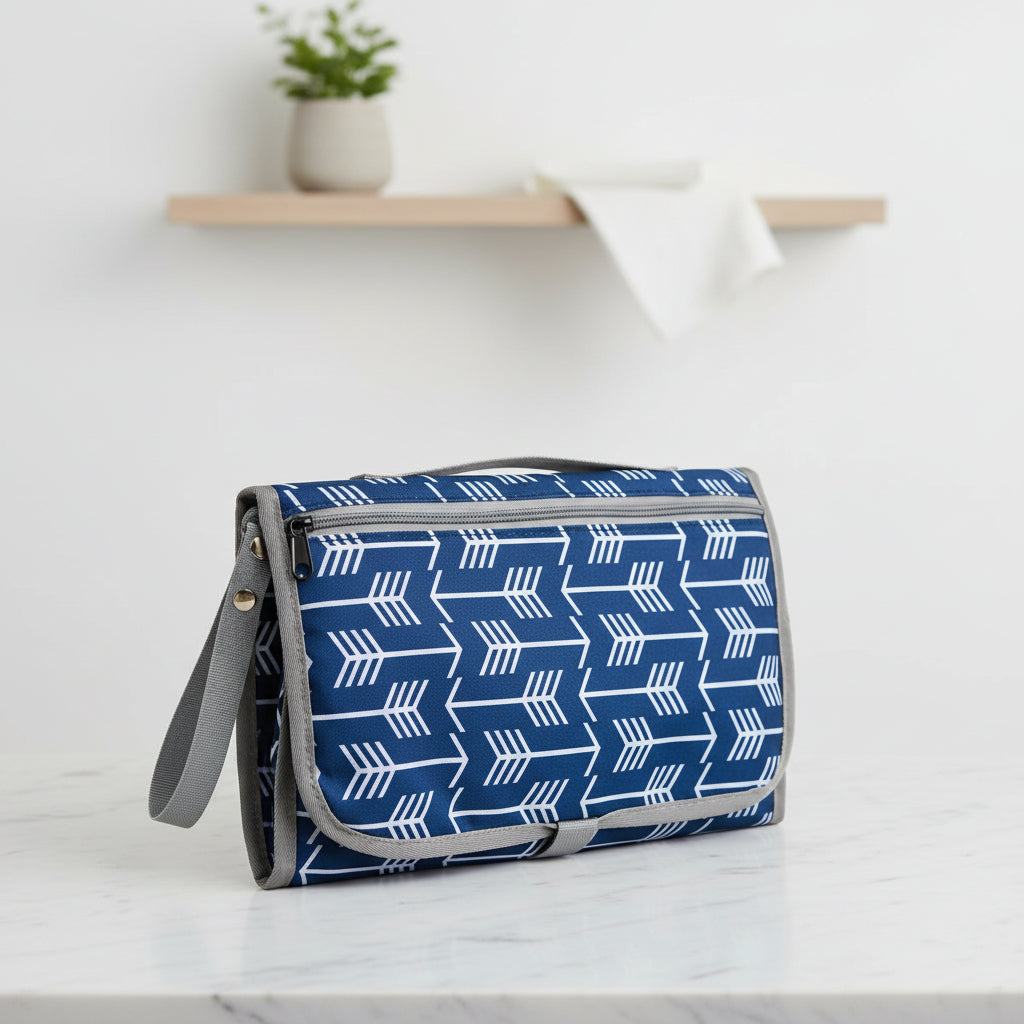 Tapis a langer portable a fermeture zippee et sangle grise, coloris bleu a fleches blanches, se glisse facilement dans tout sac de sortie.