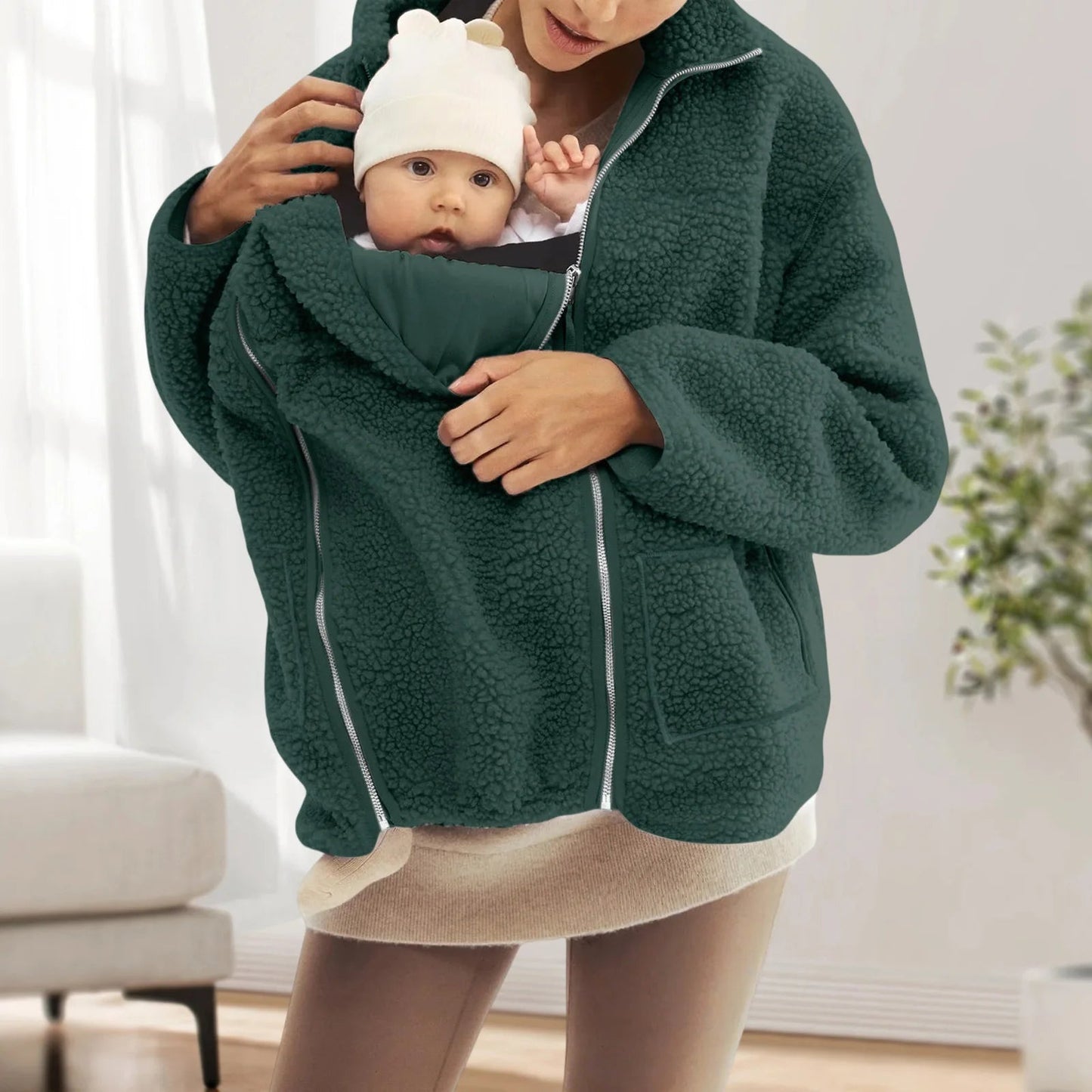 Veste de portage vert sapin utilisee a la maison, l enfant installe dans la poche frontale profite d un cocon douillet et securisant.